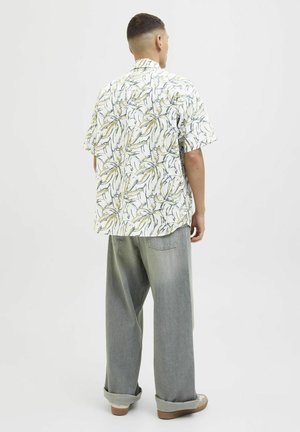 Camisa de manga corta con cuello, de base blanca, que presenta un patrón de hojas verdes y amarillas. Combinada con unos vaqueros de corte relajado en gris claro.