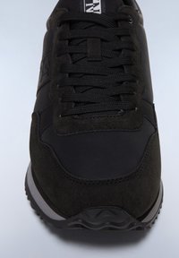 Sneaker nera caratterizzata da una combinazione di materiali in pelle e scamosciato, lacci texturizzati, colletto imbottito e suola in gomma con battistrada.