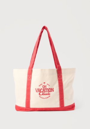 Beige canvas tote bag with red handles and trim, featuring red text "On Vacation Club" and a small palm tree logo on the front.