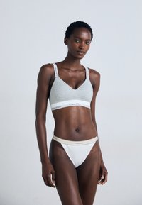 Szürke pamut bralette V kivágással, vékony pántokkal és fehér Calvin Klein logós szalaggal; hozzáillő fehér tanga bézs logós derékpánttal.