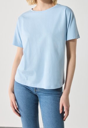 T-shirt bleu clair à manches courtes en tissu doux, avec un col rond et une coupe décontractée. Associé à un jean en denim.