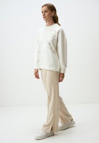 Sweatshirt blanc avec un motif de contour de fleurs, pantalon large crème et baskets blanches. Tissu lisse et coupe décontractée. Pas de détails supplémentaires.