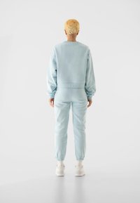 Ljusblå sweatshirt och matchande joggingbyxor i mjukt tyg. Elastiska muddare och midjeband. Vita sneakers. Enkla, avslappnade träningskläder.