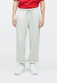 Hellgraue Jogginghose mit elastischem Bund und Kordelzug, schlicht geschnitten mit Seitentaschen, kombiniert mit weißen Sneakers.