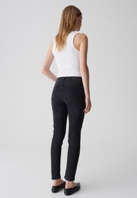 Jean skinny noir avec taille mi-haute, couture minimale et deux poches arrière, associé à un haut sans manches ajusté blanc.