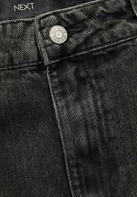Sorte denim jeans med en struktureret vævning, metalknap med "NEXT DENIM" branding og en robust talje.