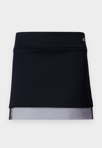 Falda negra con un top estructurado, que presenta un dobladillo de malla transparente. Acentuada con un pequeño emblema metálico en la cintura.