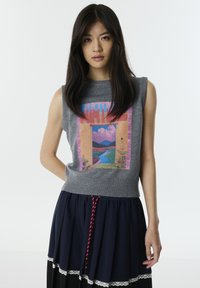 Grauer ärmelloser Pullover mit einem bunten Landschaftsdruck und einem gerippten Saum, kombiniert mit einem dunkelblauen Rock, der mit einem Spitze-Detail und einem roten Kordelzug verziert ist.