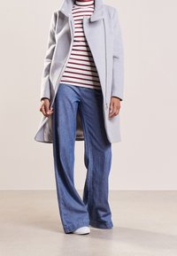 Světlě šedý kabát z vlněné směsi s vysokým límcem, doplněný červeno-bíle pruhovaným tričkem a širokými modrými džínami s rozšířenými nohavicemi. Bílé tenisky.