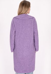 Lungo cappotto viola in material peluche e testurizzato. Presenta un ampio colletto e maniche lunghe, con una vestibilità rilassata e una lunghezza intermedia.