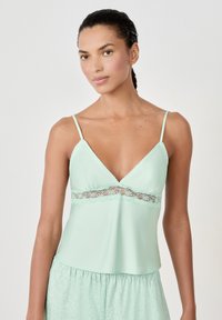 Camiseta sin mangas verde menta con trim de encaje, tirantes ajustables y un corte holgado. Textura de tela suave, escote en V y dobladillo acampanado.