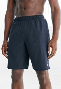 Granatowe spodenki sportowe z elastycznym paskiem w talii, gładka tekstura materiału, boczne kieszenie oraz małe logo na dole.