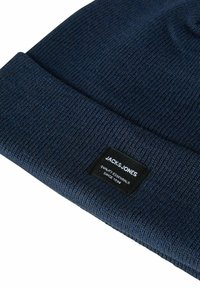 Donkerblauwe gebreide muts met opgerolde rand en een zwart rechthoekig label met de tekst "JACK&JONES Quality Essentials Since 1990."
