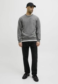 Felpa grigia con polsini e orlo a costine, indossata sopra una camicia bianca. Abbinata a pantaloni neri e scarpe nere con lacci, indossata con un berretto nero.