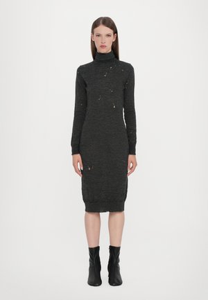 Rochie tricotată cu mânecă lungă și guler înalt, de culoare gri închis, cu o ușoară uzură, silueta ajustată și margine cu nervuri. Santici negri la glezne purtați.