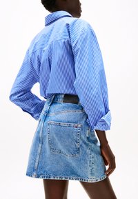 Blauw-wit gestreepte blouse met lange mouwen en een relaxte pasvorm, gecombineerd met een lichte spijkerrok met een achterzak.