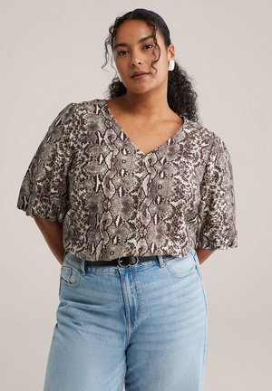 Krátká halenka s výstřihem do V, s hnědým a krémovým hadím vzorem. Kombinována s vysoce pasovanými světle modrými džínami.