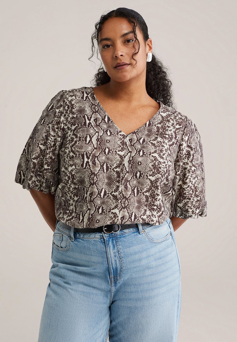 Blouse à manches courtes avec col en V, présentant un motif serpent marron et crème. Associée à un jean taille haute bleu clair.