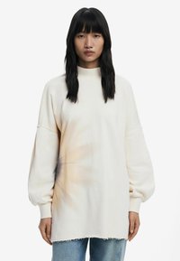 Sweatshirt oversize beige chiaro con maniche lunghe a palloncino, colletto alto e motivo tie-dye texturizzato nella parte inferiore anteriore. Orlo sfrangiato.