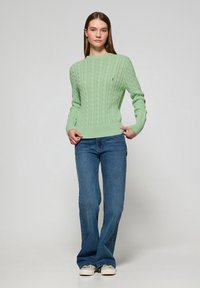 Ljusgrön stickad tröja med kabelmönster, ribbade ärmslut och nedkant. Kombinerad med blå utsvängda jeans och vita sneakers.