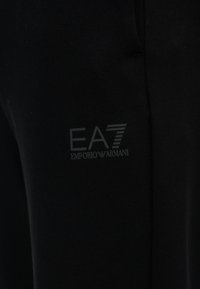 Μαύρα βαμβακερά τζόγκερ με διακριτικό λογότυπο EA7 Emporio Armani σε αντίθετο χρώμα. Το ύφασμα έχει λείο και απαλό υφή.