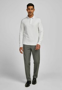 Weißes Langarm-Polohemd mit Kragen, kombiniert mit grauen strukturierten Hosen und schwarzen Schuhen, auf einem neutralen Hintergrund präsentiert.