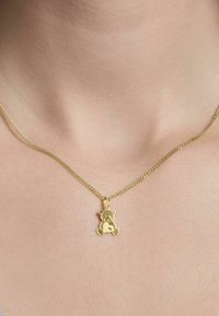 Collana d'oro con pendente a forma di orsetto. Il pendente è liscio con dettagli minimi, sospeso da una catena fine e attorcigliata.