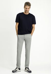 T-shirt in cotone blu navy con maniche corte, abbinato a pantaloni grigi chiari a gamba affusolata. Le calzature presentano una combinazione di colori in bianco e nero.