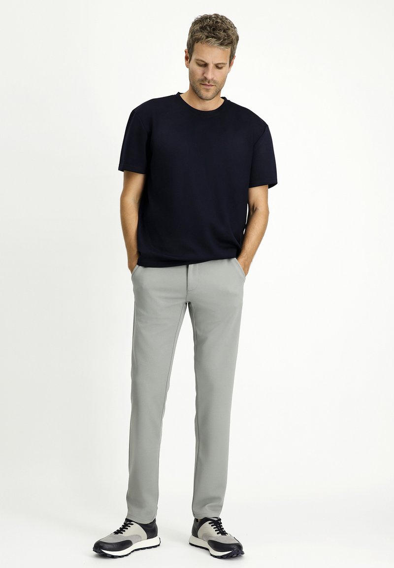 T-shirt in cotone blu navy con maniche corte, abbinato a pantaloni grigi chiari a gamba affusolata. Le calzature presentano una combinazione di colori in bianco e nero.