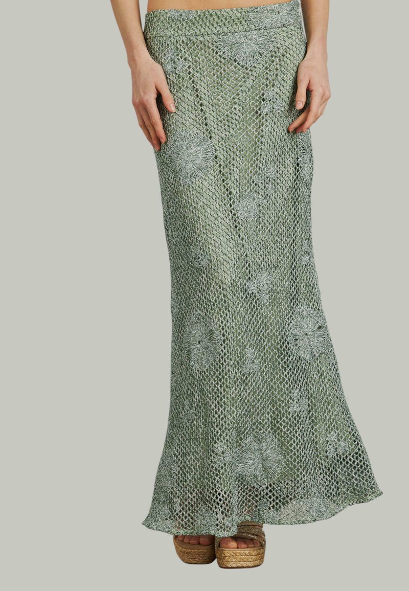 Groene gehaakte rok met bloemenpatronen, strakke taille en uitlopende zoom. Gecombineerd met tan kleurige sleehak sandalen. Doorzichtige textuur overal.