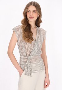 Durchsichtige Bluse in Beige mit geometrischem Muster. Mit Wickeldesign, kurzen Ärmeln und einer gebundenen Taille für eine figurbetonte Silhouette.