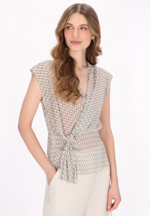 Välja blus i beige med geometriskt mönster. Har en omslagdesign, korta ärmar och knytband i midjan för en figurnära silhuett.
