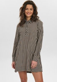Robe à carreaux noir et beige avec un col, des manches longues et un devant à boutons. Fabriquée en tissu léger, elle offre une coupe décontractée.