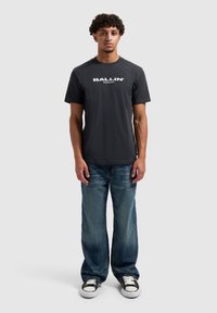 Zwart katoenen T-shirt met het witte "BALLIN'"-logo. Gecombineerd met lichtblauwe, losvallende spijkerbroek en zwart-witte sneakers.