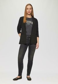 Czarna marynarka, szary T-shirt z grafiką, dopasowane czarne dżinsy i czarne płaskie buty. Gładkie tekstury i usprawniony design. Codzienny strój.