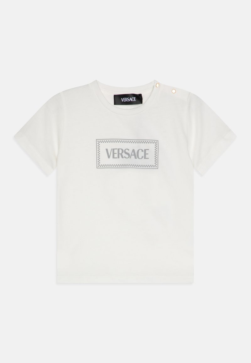 Balta medvilninė marškinėlių su trumpomis rankovėmis, kuriuose yra pilkas stačiakampis „VERSACE“ logotipo dizainas ir du auksiniai akcentiniai mygtukai kairėje peties pusėje.