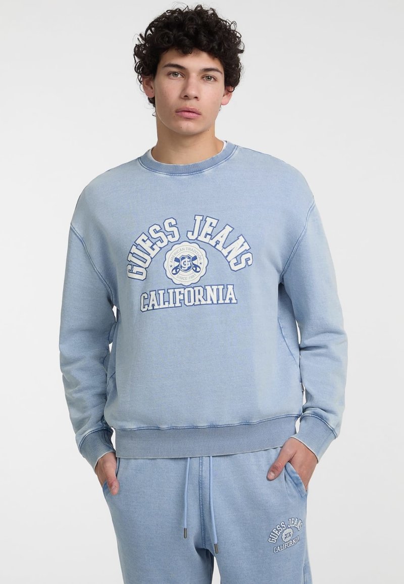 Šviesiai mėlynas apvalaus kaklo megztinis su „GUESS JEANS CALIFORNIA“ baltu tekstu. Minkšta medžiaga su nėriniuotomis rankovėmis ir apačia.