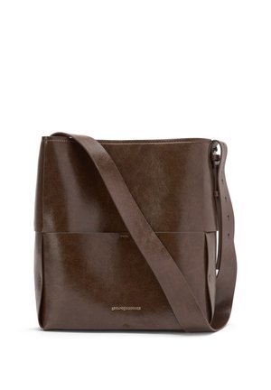 Donkerbruine leren crossbodytas met brede verstelbare riem en subtiel gouden logo-detail aan de voorkant in het midden.