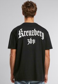 Schwarzes Baumwoll-T-Shirt mit weißem Drucktext auf dem Rücken: "Kreuzberg 361." Lockerer Schnitt mit kurzen Ärmeln und rundem Halsausschnitt.