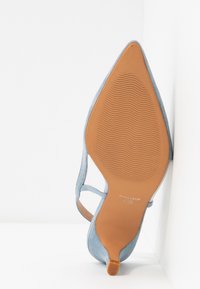 Chaussure à talon haut en suède bleu clair avec un bout pointu et un design à bande ouverte. La semelle est beige avec un motif antidérapant texturé.