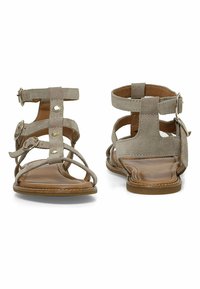 Sandali beige con cinturini, dalla finitura in morbida pelle scamosciata, suola piatta, dettagli in fibbia e design aperto davanti con molteplici cinturini incrociati.