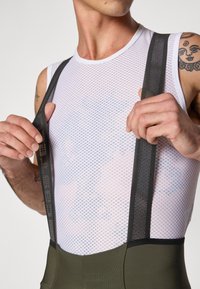 Débardeur en maille blanc avec des bretelles réglables noires, associé à un bas vert olive au design ajusté et à la texture lisse.