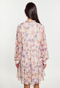 Blumenkleid aus leichtem, transparentem Stoff mit lila und orangefarbenen Blumen. Es hat lange Ärmel und ein gestuftes Rüschendesign im Rock.