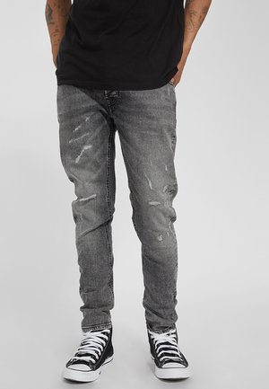 Jeans de denim gris con un corte ajustado, detalles desgastados y un suave efecto de decoloración, combinados con zapatillas altas negras.