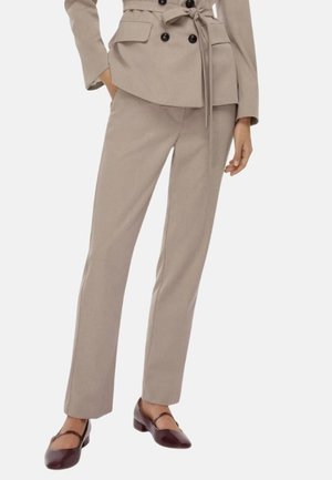Completo beige su misura con giacca doppiopetto e pantaloni abbinati. Tessuto morbido, texture liscia e scarpe basse marroni con un accento a strappo.