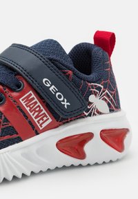 Kék és piros sneaker, amely hálós textúrával, fehér talppal és piros kiemelésekkel, valamint pókháló mintázattal rendelkezik, a "GEOX" és a "MARVEL" logóival megjelölve.