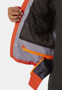 Interior de chaqueta negra con forro naranja y gris. Cuenta con un bolsillo de malla, cremallera naranja y detalles de botón texturizados para el cierre.