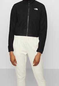 Giacca in pile nera cropped con colletto alto, chiusura frontale con zip e logo bianco. Abbinate a pantaloni con cintura elastica bianca.