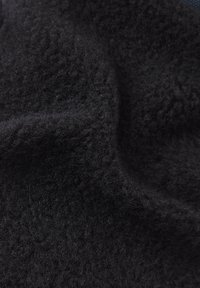Schwarzer Fleece-Stoff mit einer weichen, strukturierten Oberfläche. Das Material wirkt dick und samtig und zeigt subtile Variationen in Tiefe und Glanz.