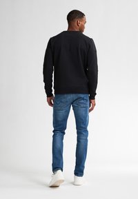 Zwarte sweatshirt met lange mouwen en ronde hals, gecombineerd met lichtblauwe jeans en witte sneakers. Het design is casual en heeft een ontspannen pasvorm.